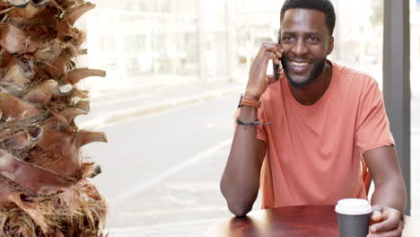 A-young-African-American-man-talks-on-his-phone-at-an-outdoor-cafe-with-copy-space