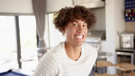 A-young-biracial-man-is-smiling-broadly-in-the-kitchen-at-home