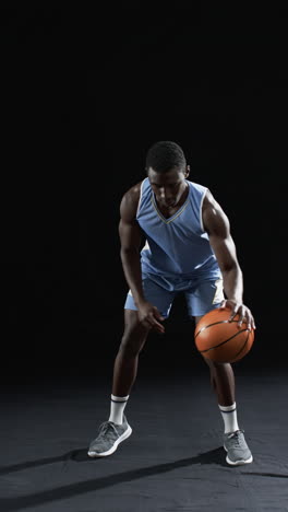 Vertical-video:-African-American-athlete-bouncing-basketball,-black-background