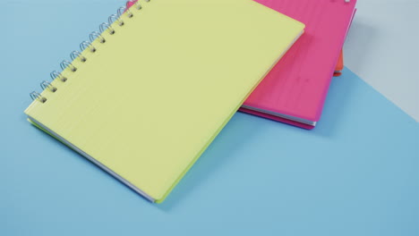 Yellow-and-pink-spiral-notebooks-overlap-on-a-blue-background,-with-copy-space