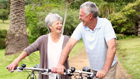 Retired-couple-standing-in-the-park-with-their-bikes