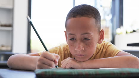 Ein-Gemischtrassiger-Junge-Mit-Sommersprossen-Konzentriert-Sich-In-Einem-Klassenzimmer-In-Der-Schule-Auf-Das-Schreiben-Mit-Einem-Bleistift