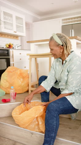 Vertical-video:-A-senior-African-American-woman-sorting-recycling-at-home