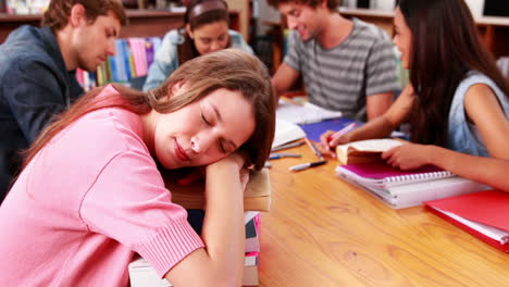 Estudiantes-Que-Estudian-Juntos-En-La-Biblioteca-Con-Una-Niña-Durmiendo-Sobre-Libros