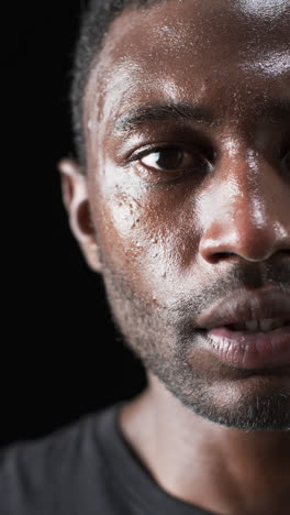 Vertical-video:-Close-up-of-African-American-male-athlete-showing-determination,-black-background