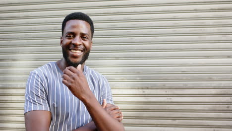 Young-African-American-man-smiles-broadly,-standing-before-a-metal-shutter-with-copy-space