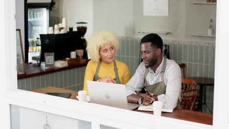 A-young-African-American-man-and-biracial-woman-talk-over-a-laptop-in-a-cafe