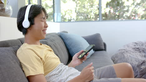 Asiatischer-College-Student-Entspannt-Auf-Der-Couch-Und-Genießt-Musik-Auf-Dem-Smartphone
