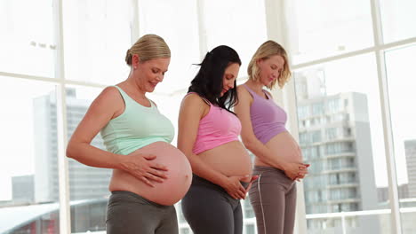 Pregnant-women-standing-in-fitness-studio-rubbing-their-bumps