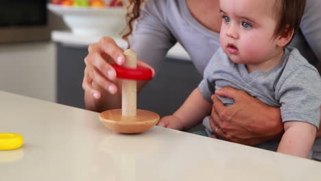 Madre-Sentada-Con-El-Bebé-En-El-Regazo-Jugando-Con-Juguetes-De-Madera