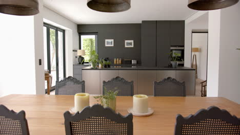 A-modern-kitchen-with-dark-cabinetry-is-viewed-from-a-wooden-dining-table
