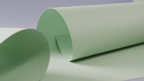 Close-up-of-two-pale-green-white-rolled-papers-on-blue-background-with-copy-space-in-slow-motion