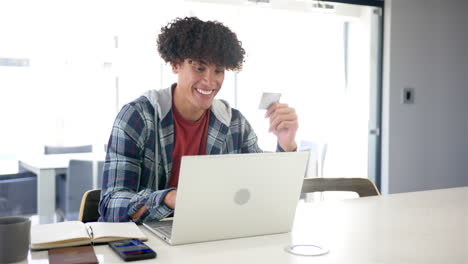 A-young-biracial-man-is-shopping-online,-using-his-laptop-and-credit-card-with-copy-space