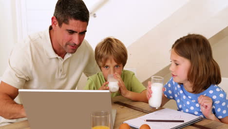 Father-and-children-using-laptop-together-at-the-breakfast-table