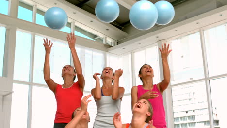 Fitness-class-smiling-at-camera-throwing-exercise-balls