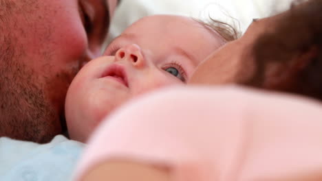 Baby-boy-in-blue-babygro-being-kissed-by-happy-parents-on-bed