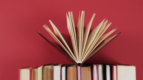 An-open-book-rests-atop-a-stack-against-a-red-background,-with-copy-space