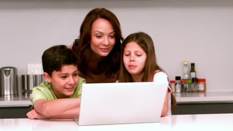 Mother-using-laptop-with-her-children-in-kitchen