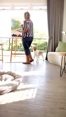 Vertical-video:-A-senior-African-American-woman-with-pet-dog-is-painting