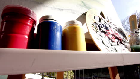 Shelf-with-colorful-paint-cans-and-palette-faces-a-canvas