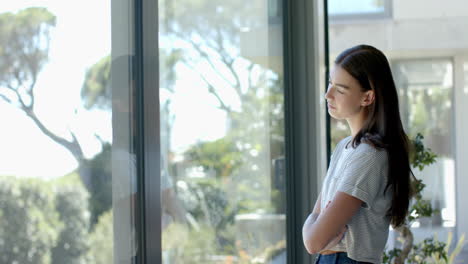 Teenage-Caucasian-girl-with-brown-hair-stands-thinking-by-a-window-with-copy-space-at-home