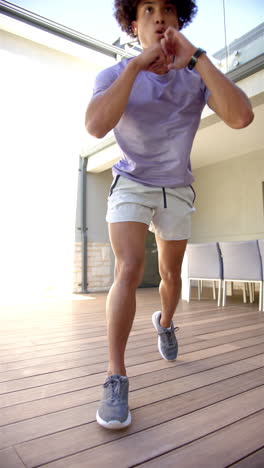 Vertical-video:-Young-biracial-male-homeowner-exercising-on-wooden-deck