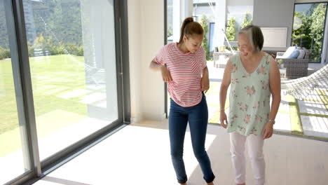 Asian-grandmother-and-biracial-granddaughter-dancing-inside-house