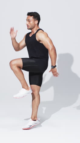 Vertical-video:-Biracial-male-athlete-running-in-place,-white-background