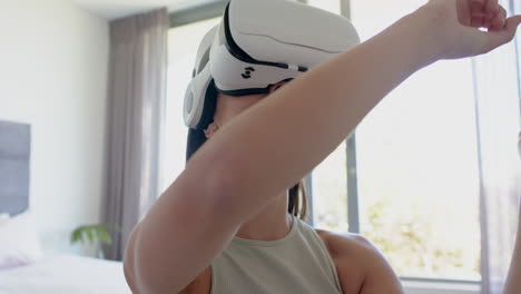 Teenage-Caucasian-girl-with-brown-hair-is-immersed-in-virtual-reality,-wearing-a-VR-headset-at-home