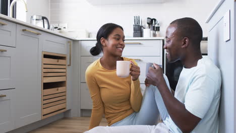A-young-African-American-couple-enjoys-a-moment-in-their-kitchen,-drinking-coffee