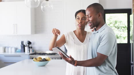 Una-Pareja-Diversa-Discute-En-Su-Cocina,-Usando-Una-Tableta