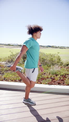 Vertical-video:-A-biracial-man-is-performing-lunges-outdoors-on-a-wooden-pathway