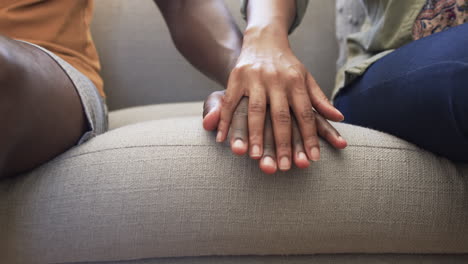 Diverse-couple-sitting-close,-hands-touching-on-sofa