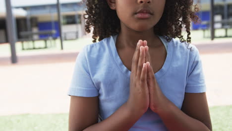 Biracial-girl-in-blue,-hands-together,-focuses-at-school