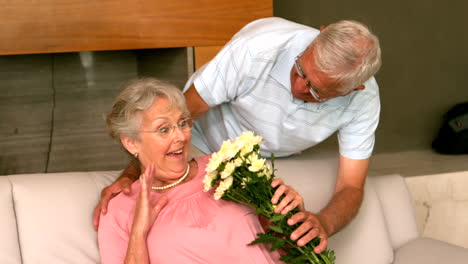 Senior-man-surpising-partner-with-flowers-on-the-couch
