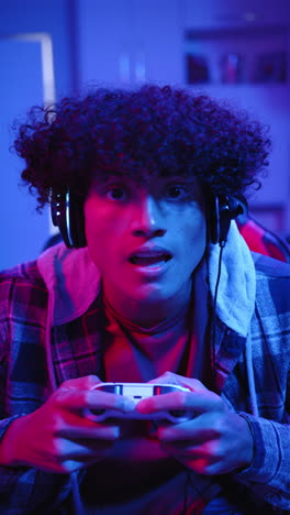Vertical-video:-Young-biracial-male-homeowner-playing-video-games,-blue-background
