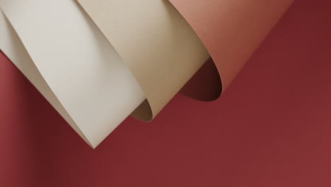 Close-up-of-three-shades-of-brown-rolled-papers-on-red-background-with-copy-space-in-slow-motion