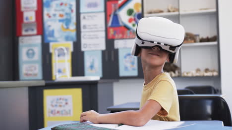 Biracial-boy-wearing-a-VR-headset-sits-at-a-school-desk-with-copy-space,-in-a-classroom-at-school