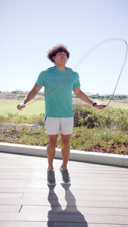 Vertical-video:-A-young-biracial-man-skipping-rope,-blue-sky-background