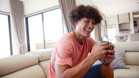 A-young-biracial-man-is-smiling-at-his-smartphone-on-the-couch-at-home