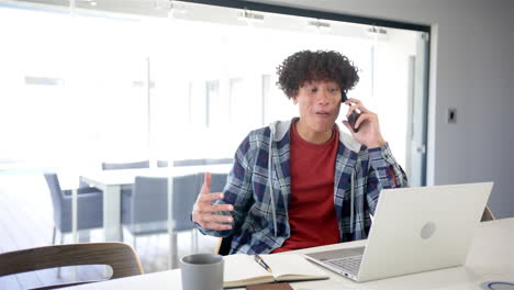 Un-Joven-Birracial-Está-En-Una-Llamada-Telefónica,-Usando-Una-Computadora-Portátil-Con-Espacio-Para-Copiar