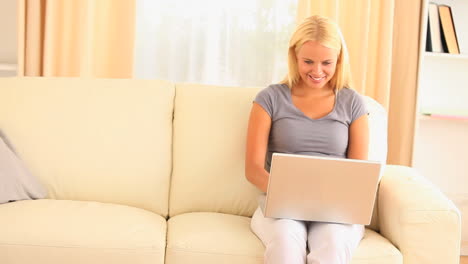 Blonde-woman-sitting-on-a-sofa-while-working-on-laptop-