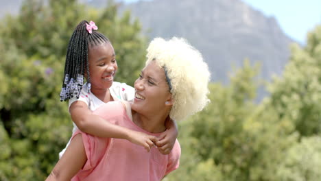 A-young-biracial-mother-with-blonde-hair-carries-an-African-American-daughter-on-her-back
