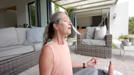 Caucasian-woman-with-grey-hair-meditating-on-patio