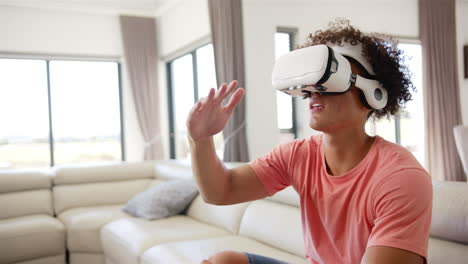 A-young-biracial-man-is-engaged-with-a-VR-headset-on-a-couch-at-home