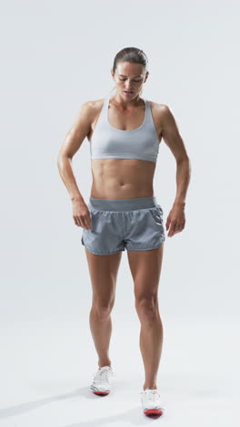 Vertical-video:-Caucasian-female-athlete-standing,-looking-down,-white-background