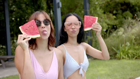 Two-young-biracial-female-friends-enjoy-watermelon-slices-outdoors