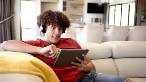 A-young-biracial-man-is-using-his-tablet-on-a-couch-at-home