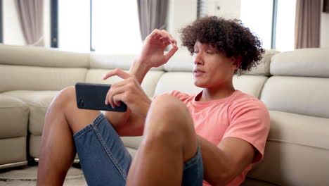A-young-biracial-upset-and-stressed-man-with-curly-hair-is-seated,-holding-a-smartphone