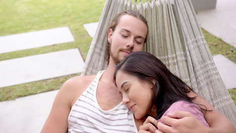 A-young-diverse-couple-relaxes-in-a-hammock-in-the-backyard-at-home
